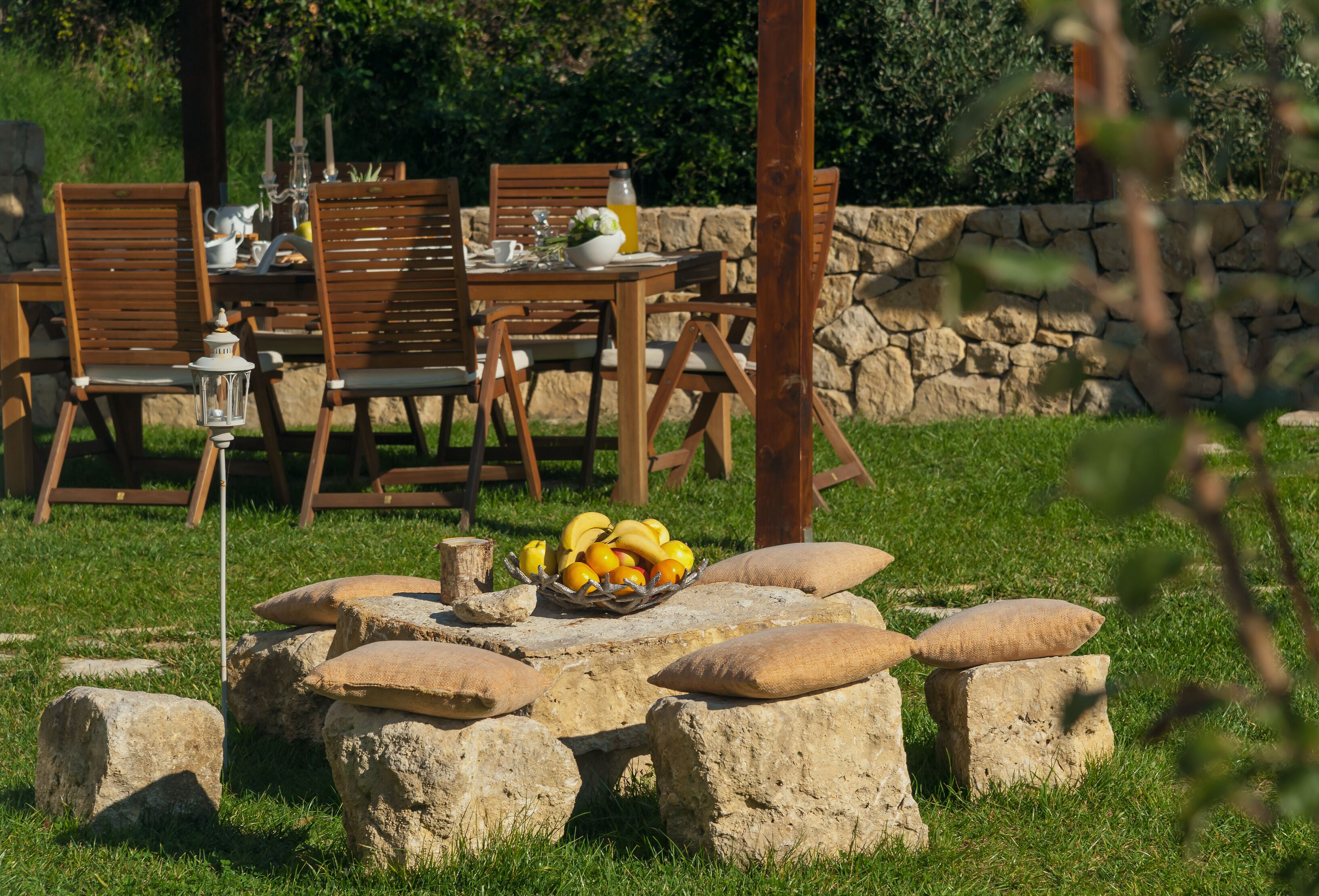 Un área de comedor al aire libre con asientos de piedra y una mesa dispuesta con fruteros, velas y una jarra.