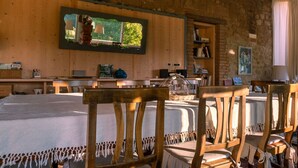 Une pièce rustique aux murs en bois, un grand miroir reflétant la vue sur un jardin, une table à manger avec des chaises et une bibliothèque.