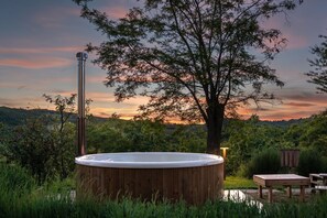Un bain à remous entouré d’une végétation luxuriante et d’un grand arbre, le tout se détachant sur le ciel au coucher du soleil.