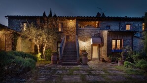 Un bâtiment en pierre avec un escalier menant à une porte, entouré de plantes en pot et bordé d’un chemin pavé.