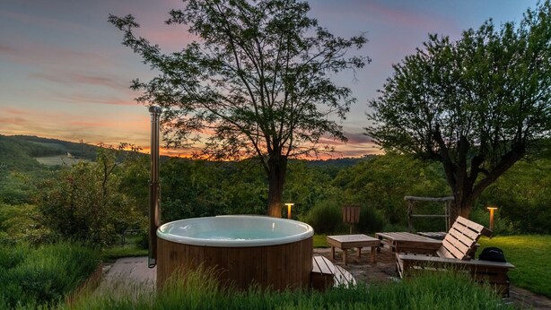 Un bain à remous entouré de meubles en bois et d’arbres, le tout situé dans un cadre pittoresque avec une vue imprenable sur une colline.