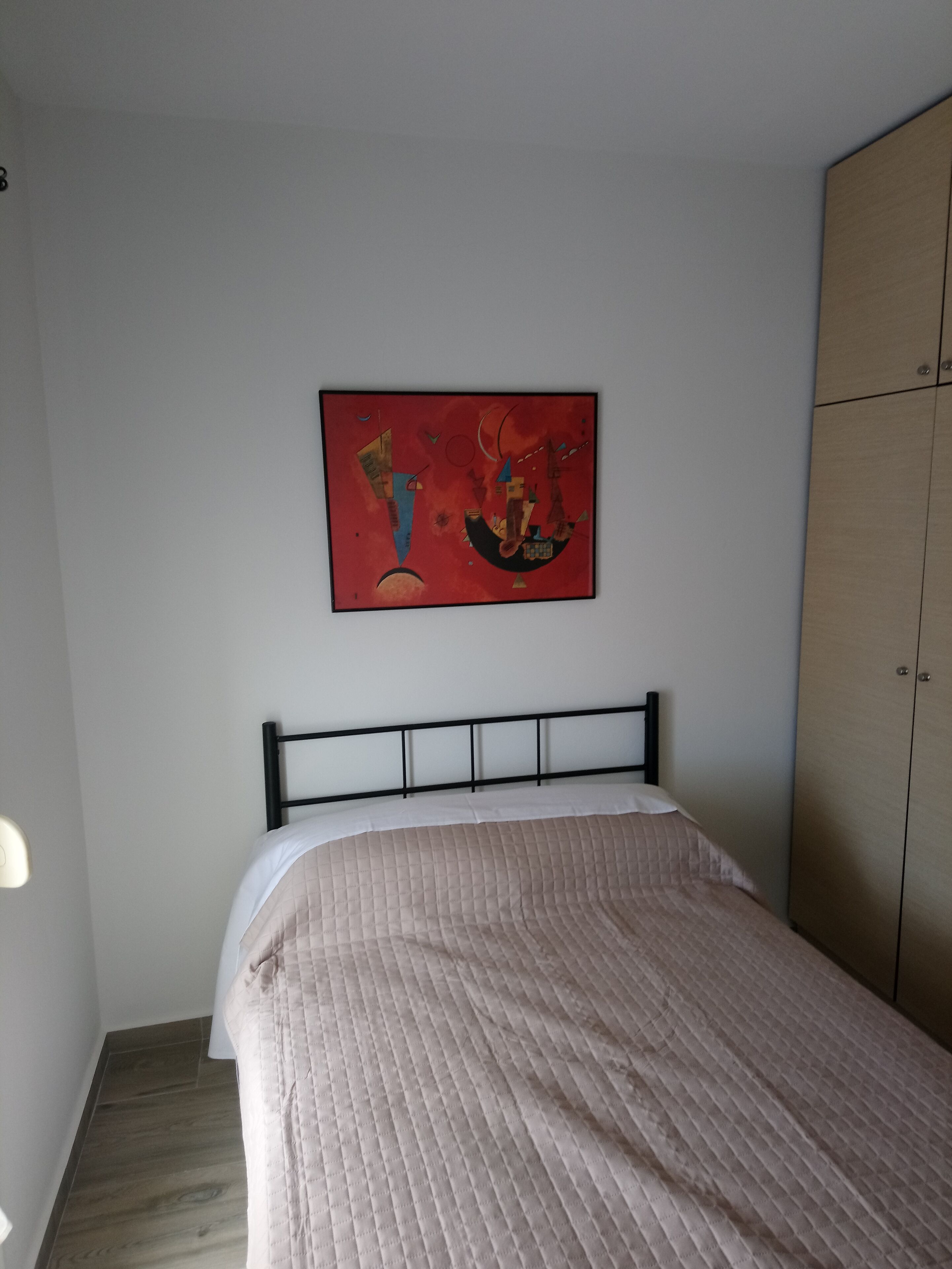 A bedroom with a bed, a wall-mounted painting, and a wardrobe.