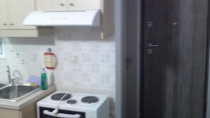 A kitchen with white cabinets, a stainless steel sink, a white stove, and a door with a silver handle. - Limena's penthouse apartment (Limenaw Hersonisou Crete)