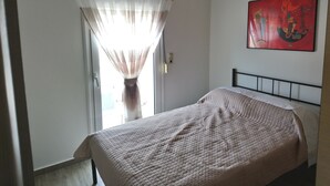 A bedroom with a bed, a window with sheer curtains, a wall-mounted painting, and a door. - Limena's penthouse apartment (Limenaw Hersonisou Crete)