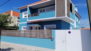 A two-story residential building with a blue facade, a red-tiled roof, and a gated entrance.