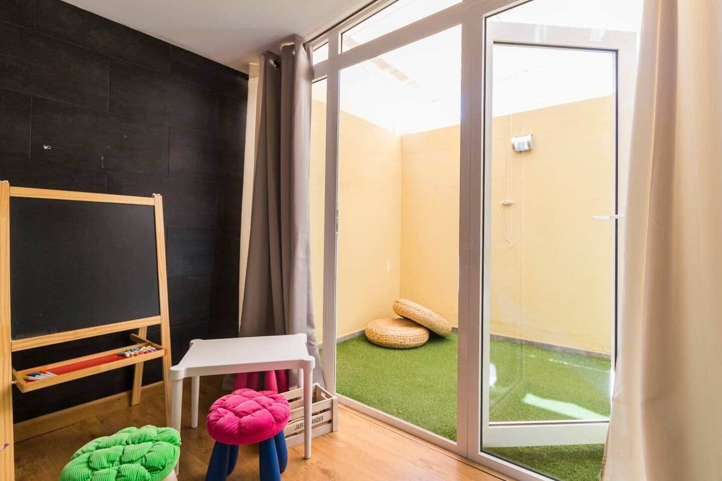Een kamer met een zwarte wand, een witte tafel, een roze stoel, een groene stoel en een houten plank met boeken.