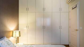Een slaapkamer met een bed, nachtkastje, lamp, kledingkast en een deur.