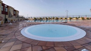 Una piscina con borde de baldosas, rodeada de sombrillas y un flotador salvavidas.