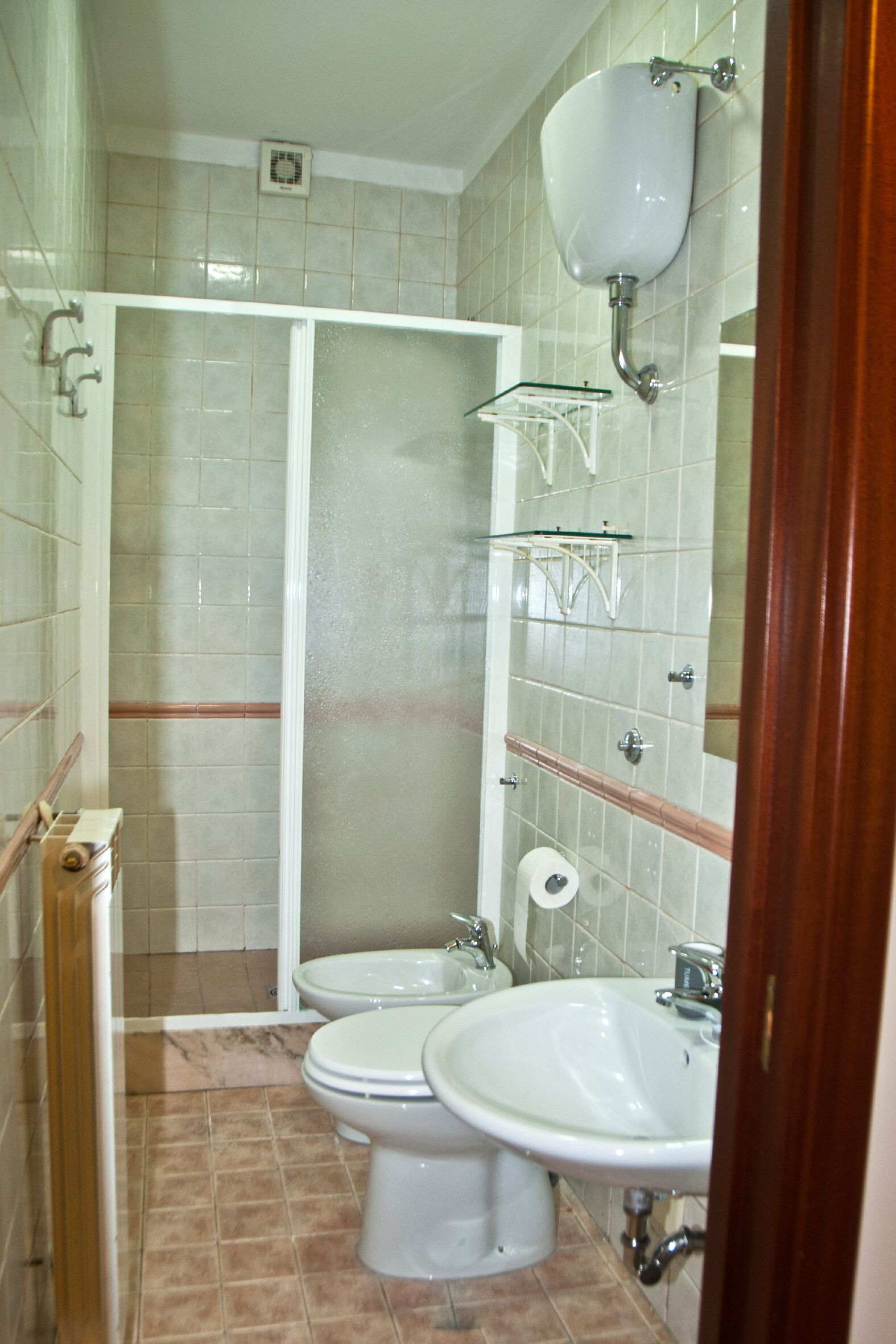 A bathroom with a shower, two toilets, a sink, and a mirror.