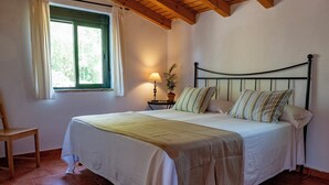 A bedroom with a bed, a nightstand, a lamp, a chair, and a window with curtains.