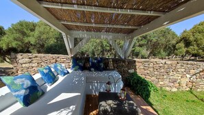 A covered outdoor seating area with a stone wall backdrop, cushioned seating, and a wooden deck.