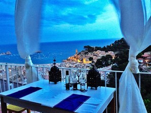 A table set for two with a view of a coastal town at dusk.