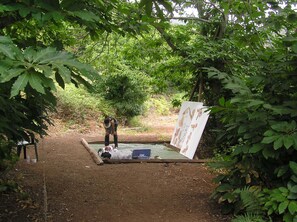 Una instalación artística al aire libre con una pintura sobre lienzo, rodeada de árboles y un sendero de tierra.