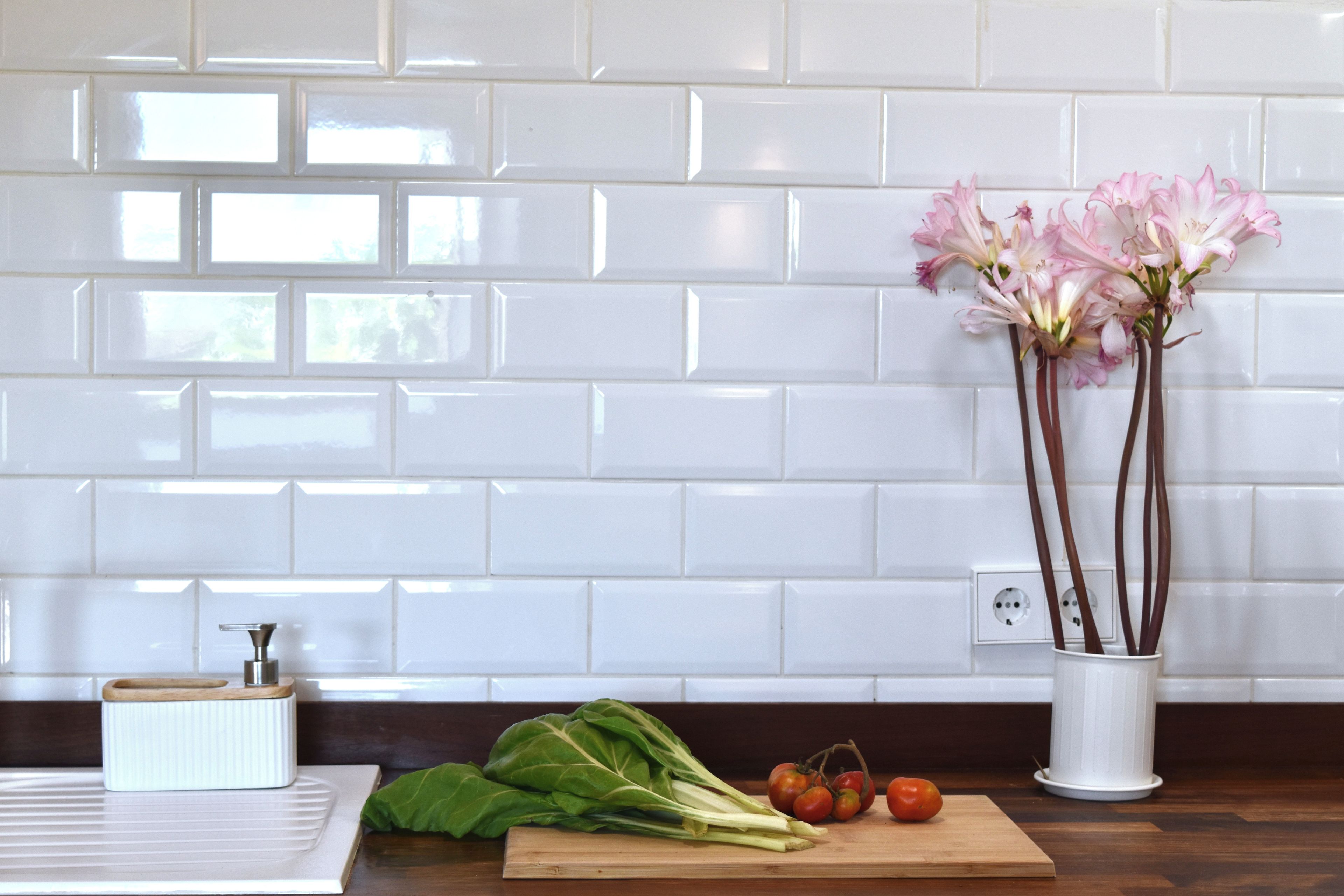 A kitchen counter with a cutting board, leafy greens, tomatoes, and a vase with flowers.
