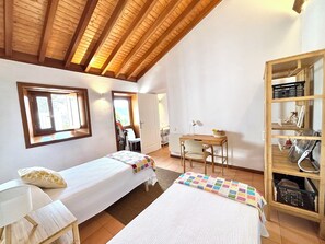A room with two single beds, a desk, a chair, and a shelving unit.