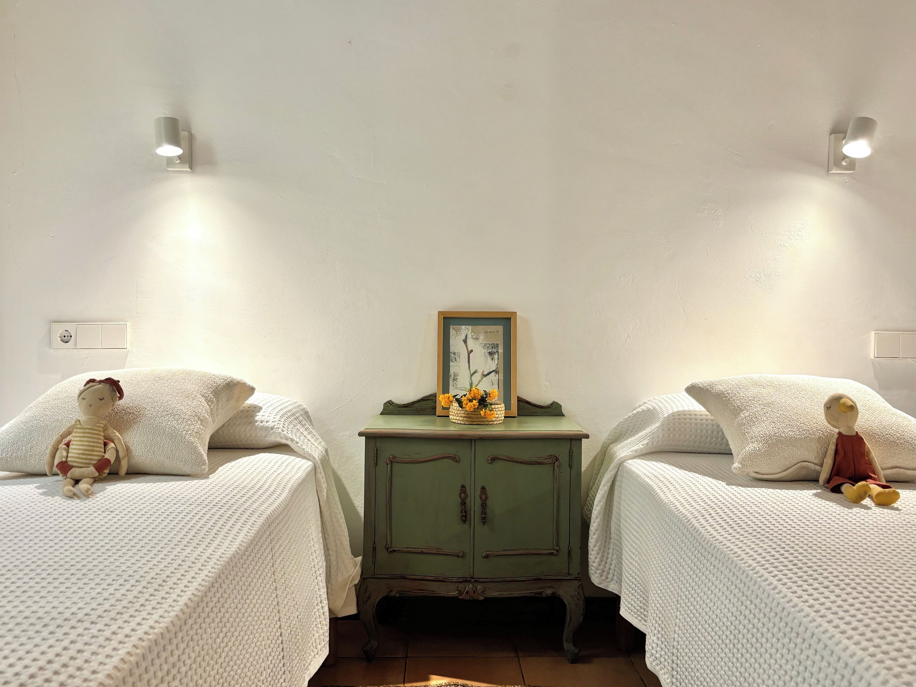 A room with two beds, a green dresser, and wall-mounted lights.