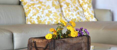 A wooden box with flowers on a glass table in a living room with a sofa and patterned cushions.