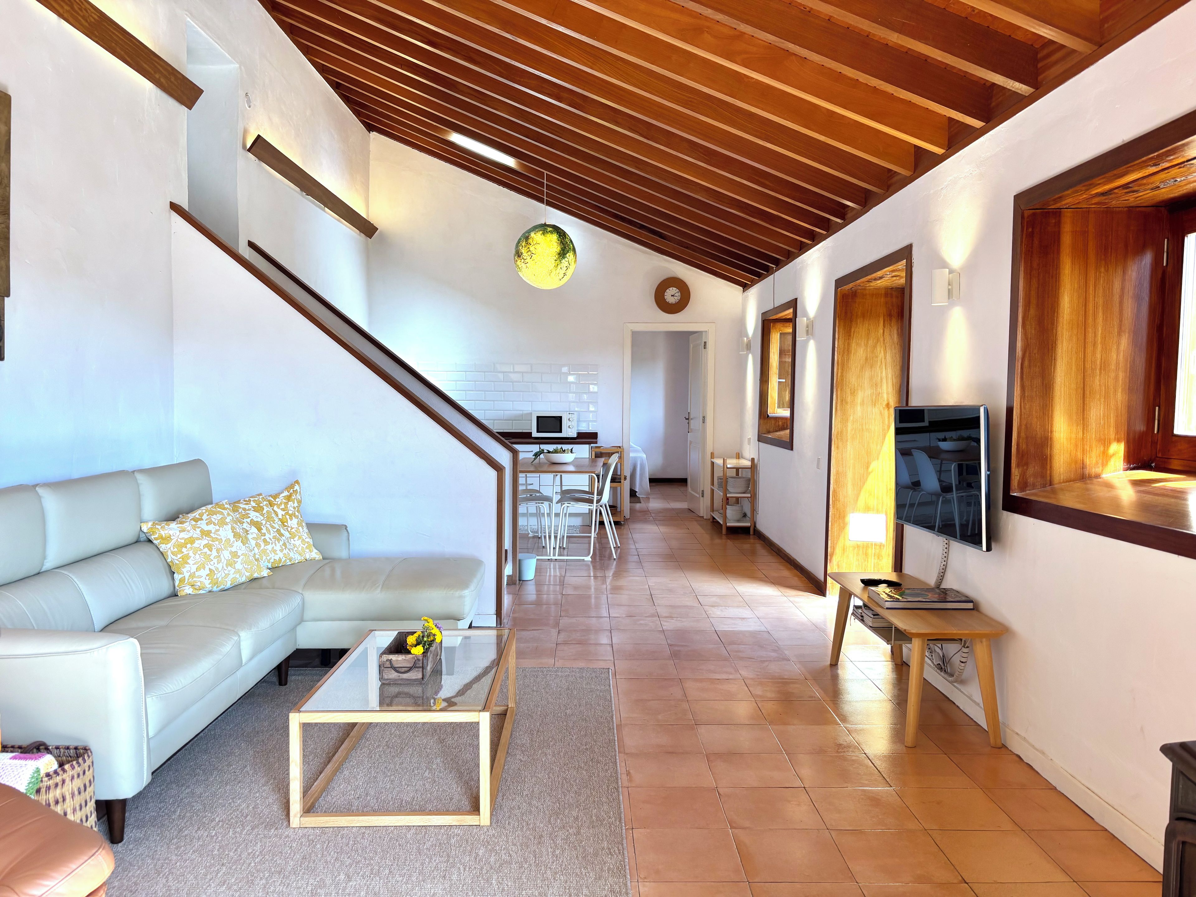 A modern living room with a glass coffee table, a sofa, and a TV mounted on the wall.
