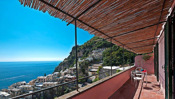 Un balcón con vista al mar y a un pueblo en la ladera.