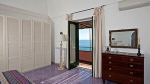 Un dormitorio con vista al mar, un aparador de madera, un espejo y una cama con manta a rayas.