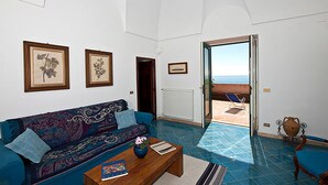 Salón con sofá, mesa de centro y vista al mar a través de una puerta abierta.