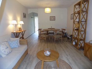A cozy living room with a sofa, a coffee table, a dining table with chairs, and a bookshelf.