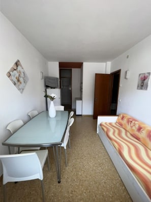 Un espacio habitable compacto con mesa y sillas de comedor, un sofá, una kitchenette y una puerta que da a otra habitación.