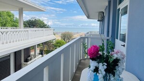 Uma varanda com corrimão branco, um arranjo de flores e vista para a praia e o oceano.