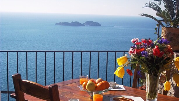 A wooden table with breakfast items, a vase of flowers, and a view of the sea and islands. - Villa Vanessa with Private Pool, Terrace, Sea View and parking near Positano (Vico Equense)