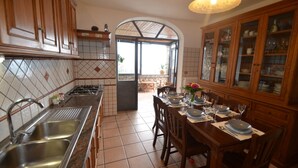 A kitchen with a tiled backsplash, wooden cabinets, a dining area with a table set for four, and a view through an arched doorway to an outdoor area. - Villa Vanessa with Private Pool, Terrace, Sea View and parking near Positano (Vico Equense)