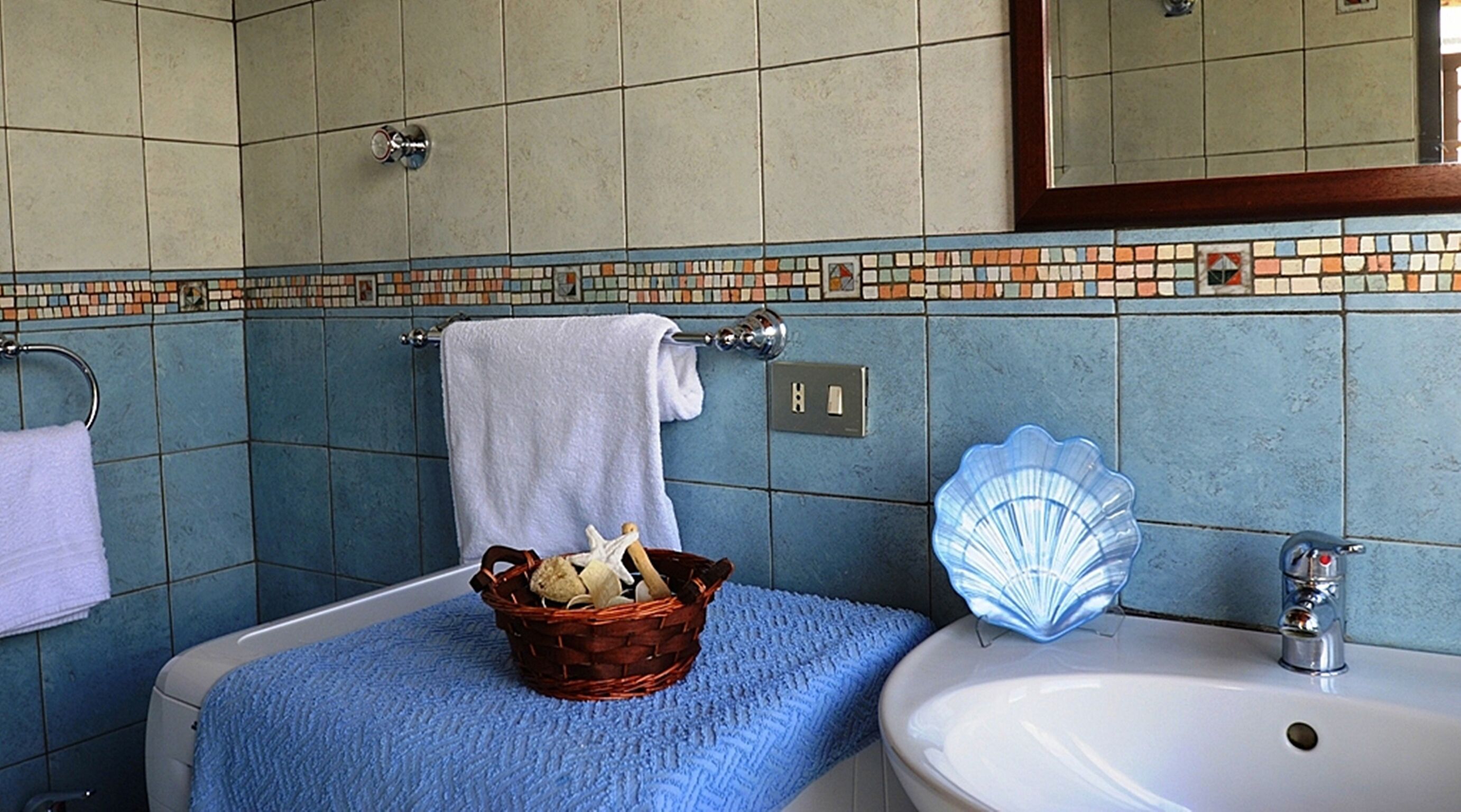 Een badkamer met een badkuip, een wastafel en een spiegel. Er is een handdoekhouder met een witte handdoek en een mand met toiletartikelen.