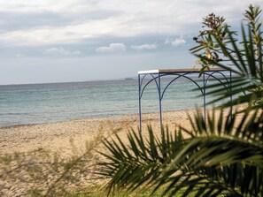 A beach with a metal table structure and palm fronds in the foreground.