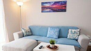 A living room with a sofa, a coffee table, a lamp, and a painting on the wall. - Appartment 51 sq.m / Sandy beach + Int. Airport (Saronida)