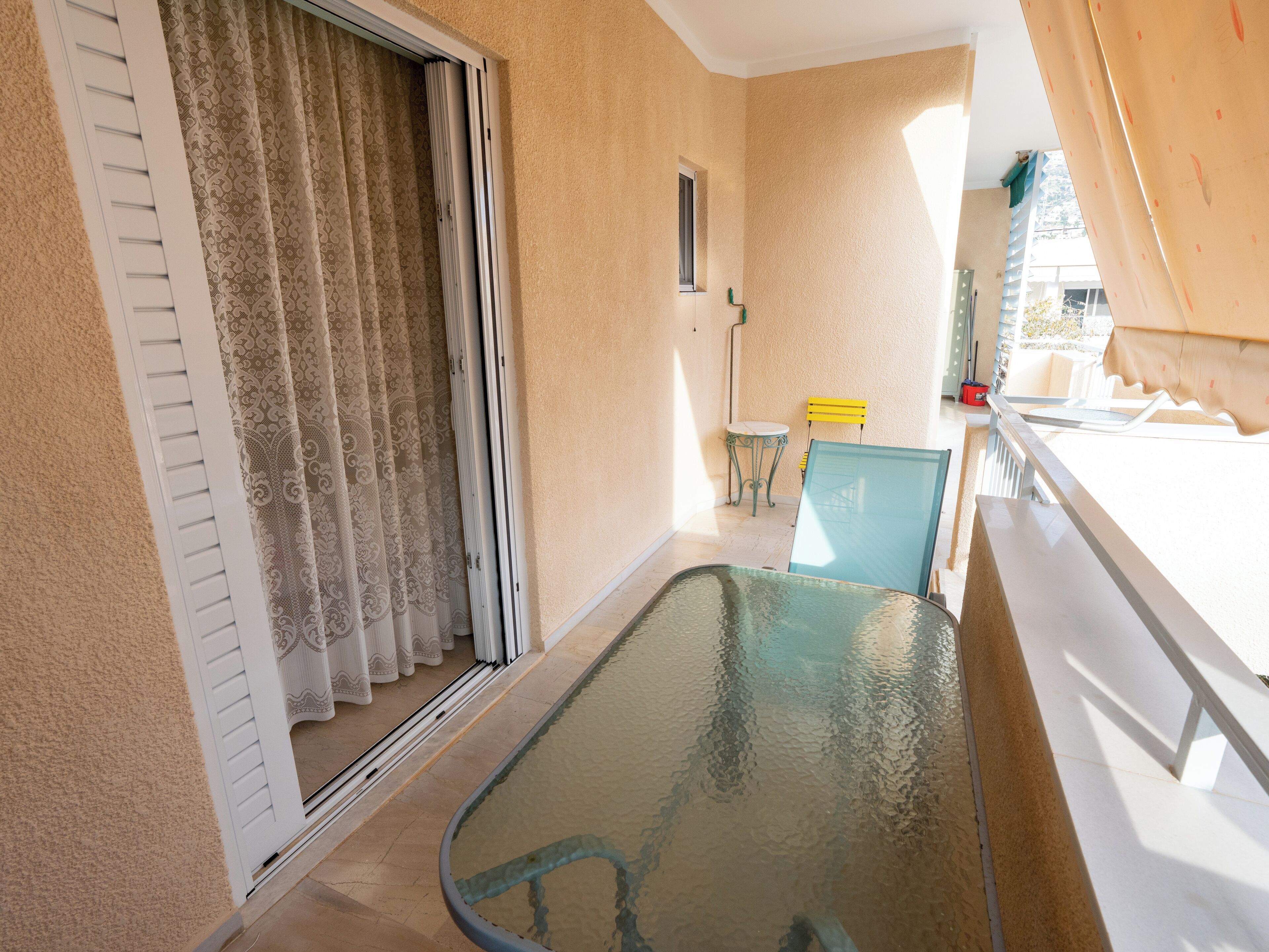 Ein Balkon mit Glastisch, einem Stuhl und einem kleinen Tisch mit gelbem Stuhl.