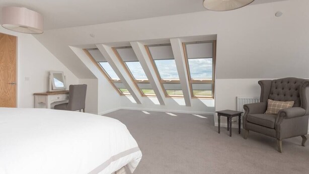 Ein Schlafzimmer mit einem großen Bett, einem Schreibtisch, einem Sessel, einem kleinen Tisch und einem Fenster mit Blick.