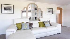 Ein weißes Sofa mit vielen Kissen, ein großer Spiegel und gerahmte Bilder an der Wand.