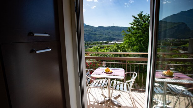 Un balcon avec une table et des chaises, une vue sur un paysage montagneux et une porte vitrée donnant sur une pièce avec un placard.