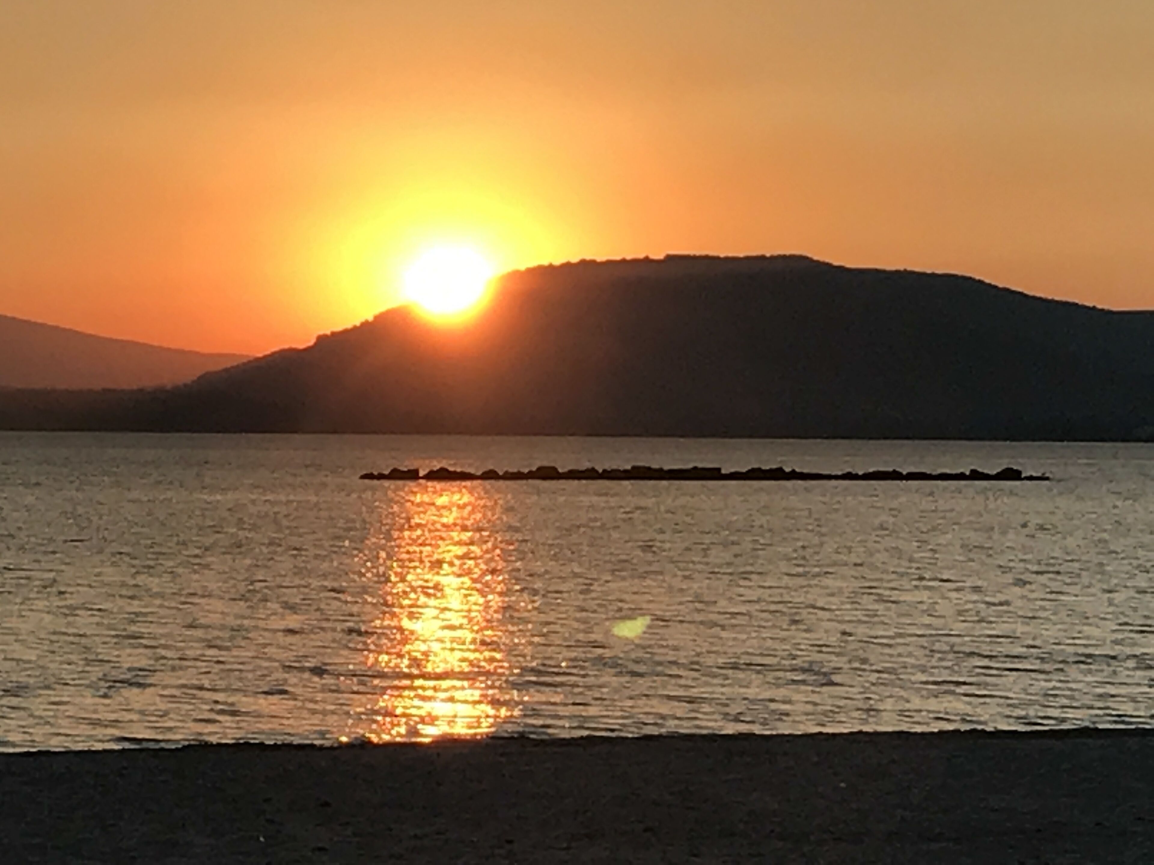 Un coucher de soleil sur une étendue d’eau calme, avec une masse terrestre visible au loin.