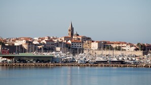 A marina with numerous boats docked, a prominent tower, and buildings with red-tiled roofs in the background. - Cozy and spacious apartment (Alghero)