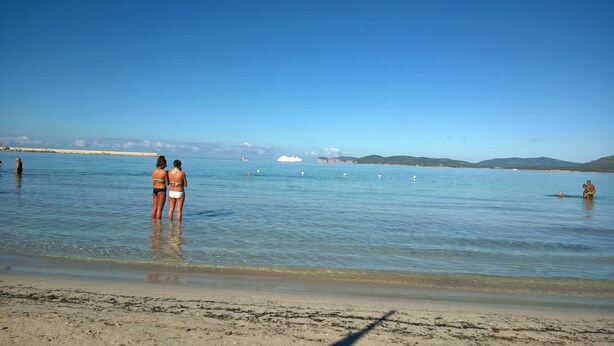 A beach with clear water, a sandy shore, and distant mountains. - Cozy and spacious apartment (Alghero)