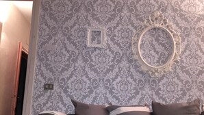 Um quarto com papel de parede estampado, um sofá escuro com almofadas listradas e um espelho decorativo na parede.