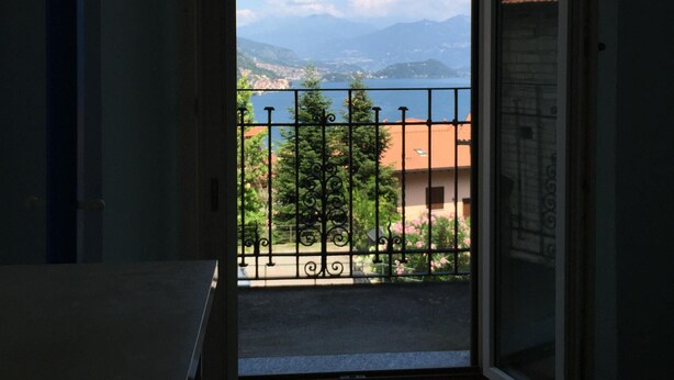 Quarto com vista para uma paisagem montanhosa e um corpo d'água a partir da varanda.