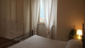 Quarto com cama, radiador, janela com cortinas, guarda-roupa e abajur.