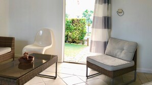 Una habitación con una mesa de vidrio, sillas de mimbre y vistas a un jardín a través de un ventanal corredero.