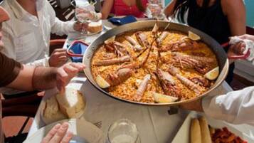 Un plato de paella en una mesa con gente alrededor.