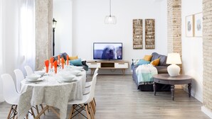 Uma sala de estar moderna com área de jantar, televisão e parede de destaque em tijolo.