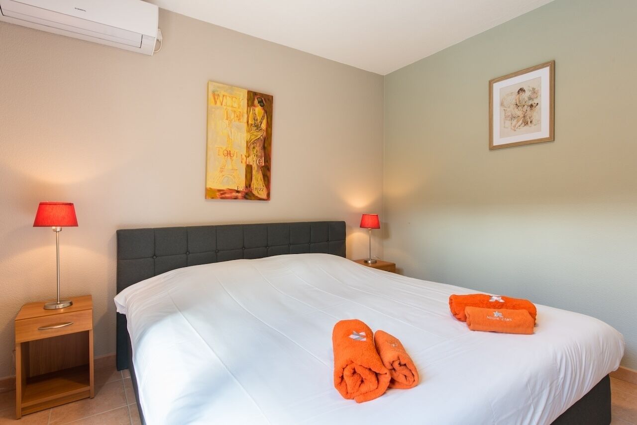 Hotelkamer met een groot bed, twee nachtkastjes met lampen, een wandairconditioner en kunstwerken.