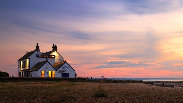 Een wit gebouw met een bord waarop 'Old Coptune' en 'Stable Bay' staat, in de zonsondergang.