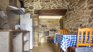 A narrow kitchen with stone walls, a wooden ceiling, and a table with a checkered tablecloth. -   Casa do Comediante - Apartment 2 + 1 (San Xoán de Río)