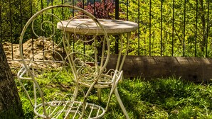 A metal chair with a round table in a garden with a fence and trees. -   Casa do Comediante - Apartment 2 + 1 (San Xoán de Río)